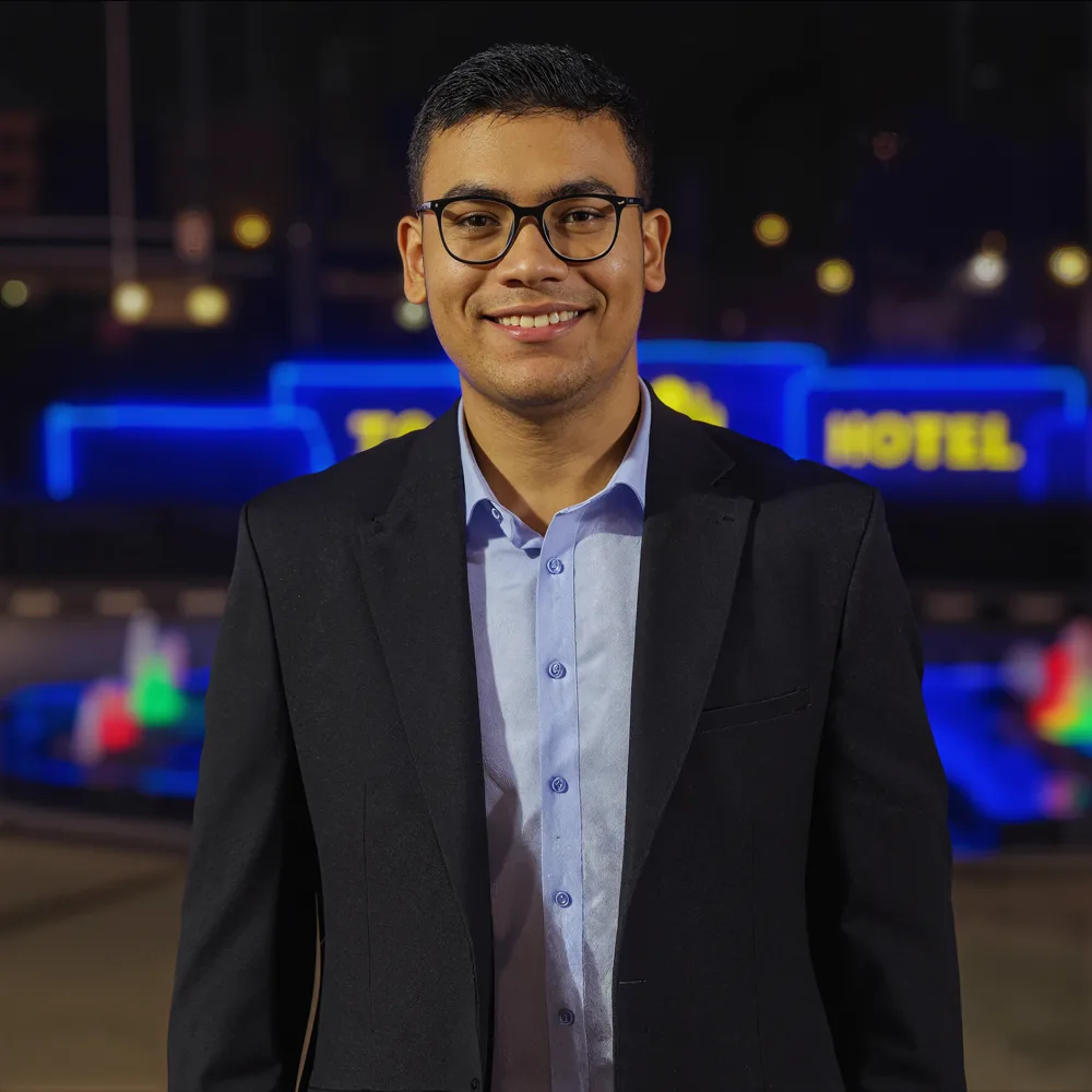 Portrait of Saad in a dark blazer and glasses, smiling